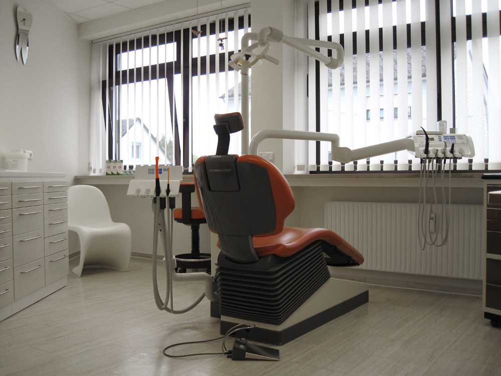 Rückansicht eines Zahnarztstuhls mit rotem Bezug im Behandlungszimmer.