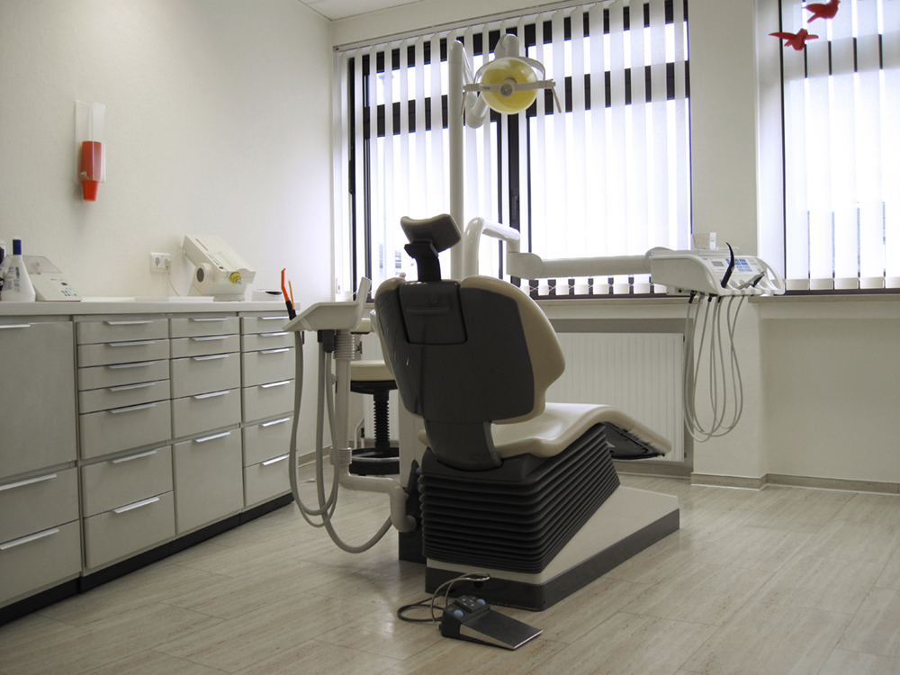 Rückansicht eines Zahnarztstuhls mit weißem Bezug im Behandlungszimmer.